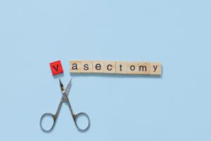  the word vasectomy made with wooden tiles on a blue background; V is red and scissors are under the word