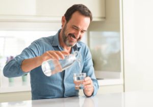 Middle age man drinking a glass of water with a happy face