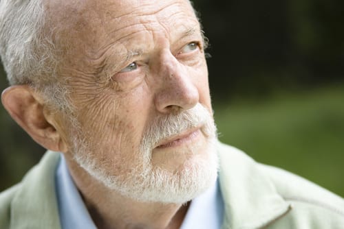 A headshot of an elderly man with white hair and beard, looking up at an angle. He's outdoors