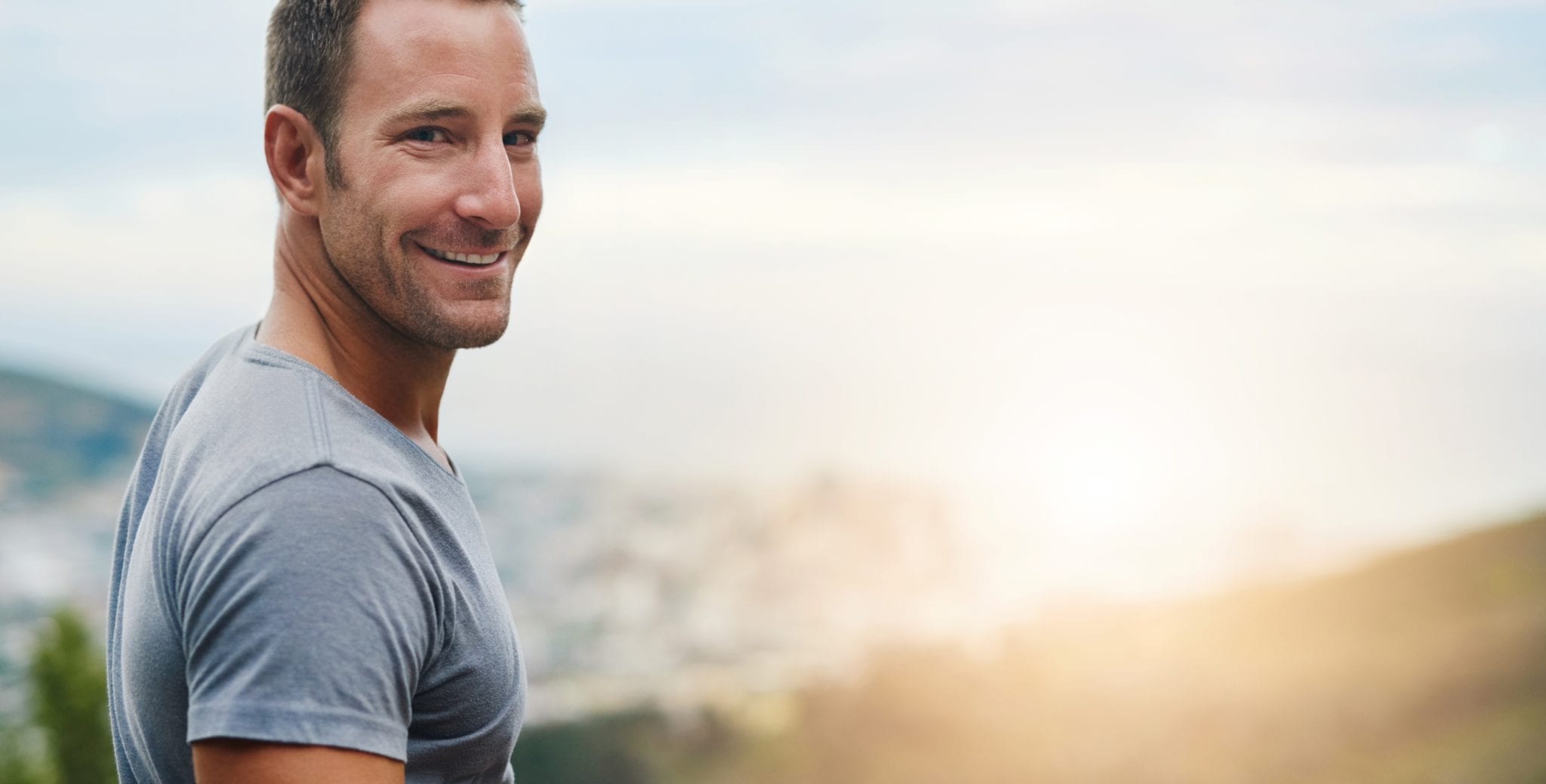 Headshot of man looking back at camera with skies and montains in the background as he is smiling widely