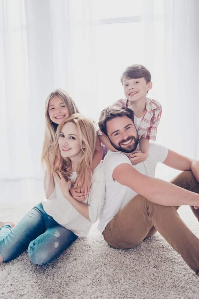 Parents seated on the floor with their children behind them, all smiling and posing for photograph