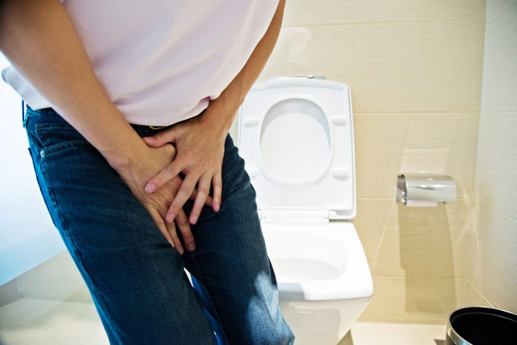 Man with hands holding his crotch by a toilet. He is diagnosed with urinary incontinence.