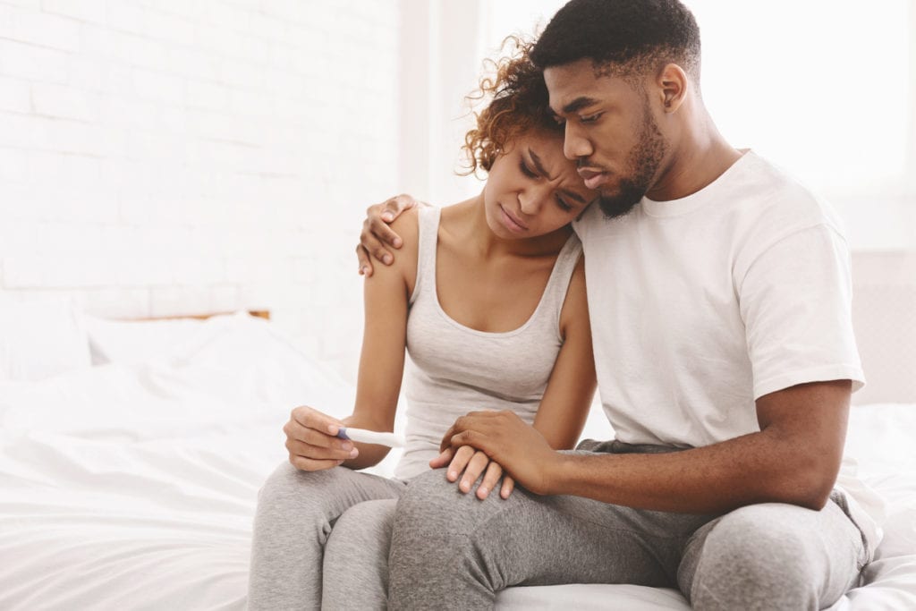 Man holding woman seated on edge of bed