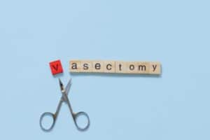  the word vasectomy made with wooden tiles on a blue background; V is red and scissors are under the word