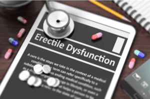Tablet with Erectile Dysfunction on screen, stethoscope, pills and objects on wooden desktop