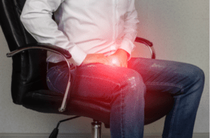 A man sits in an office chair and holds on to the groin in pain