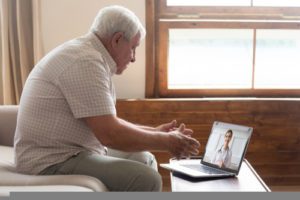 Elderly 70s man seated on sofa make distant video call